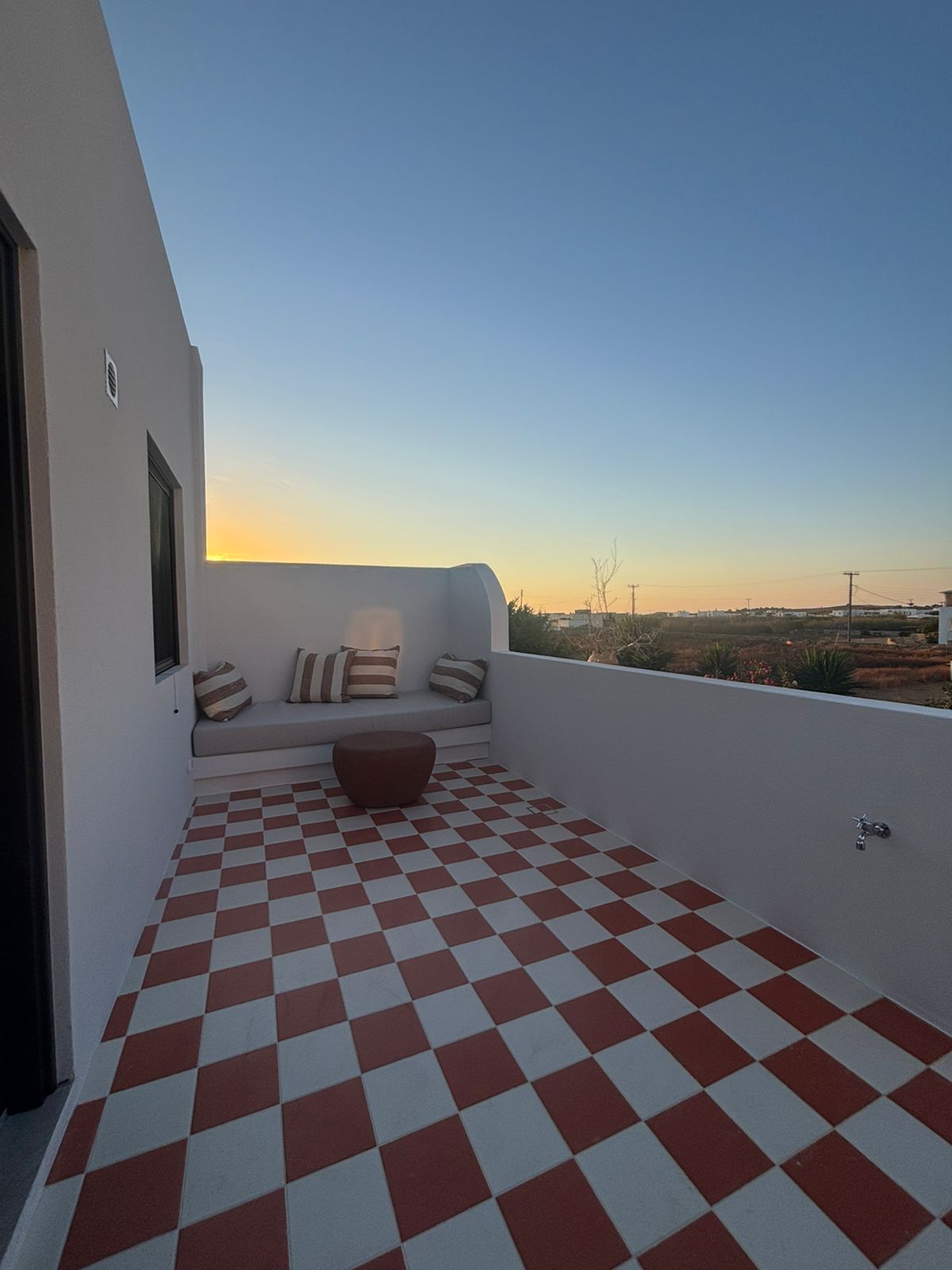 Private terrace with red-and-white checkerboard tiles and built-in bench at sunset, Bluewaves Antiparos Sunstone Terrace House