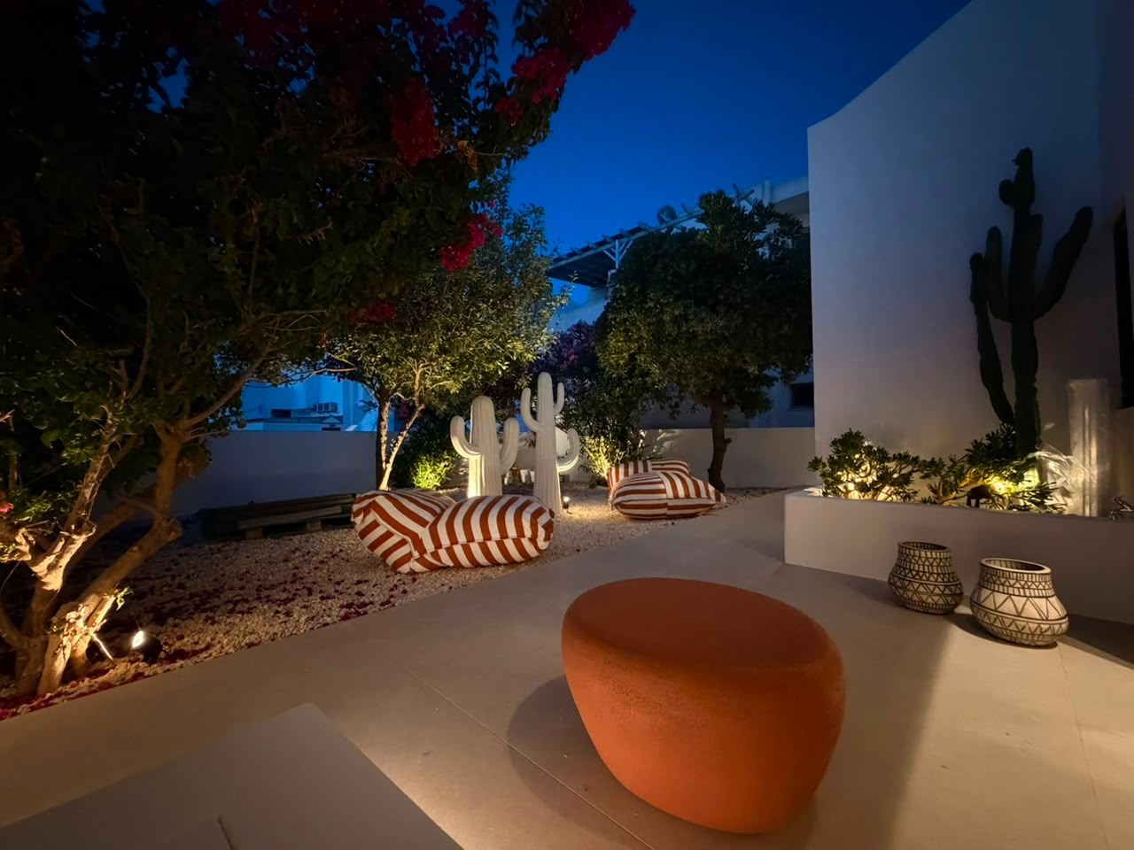 Illuminated private garden with bougainvillea, cactus sculptures and striped loungers at Bluewaves Antiparos Moonstone Jacuzzi House